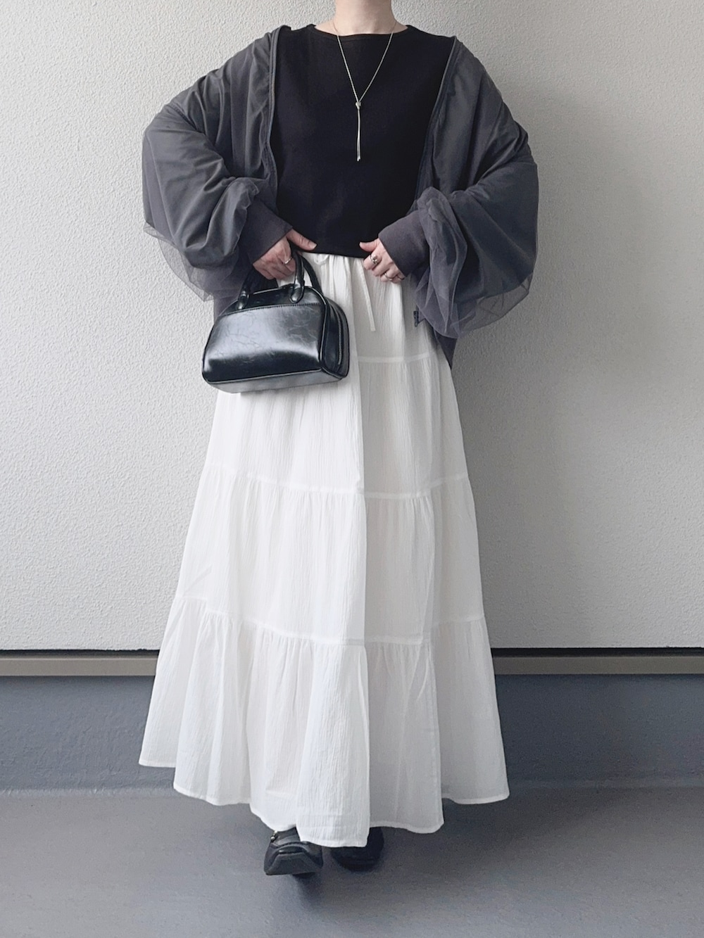 グレー系のブルゾン、ブラック系のTシャツ/カットソー、ホワイト系のスカートを着用したレディースの春コーディネートの2枚目の写真