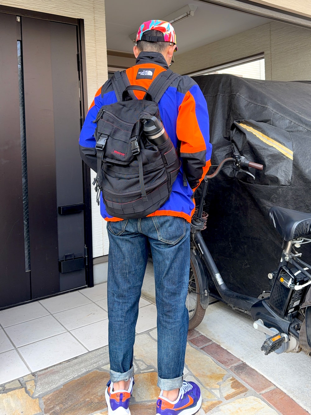 オレンジ系のナイロンジャケット、ブルー系のデニムパンツ、パープル系のスニーカーを着用したメンズの冬コーディネートの2枚目の写真