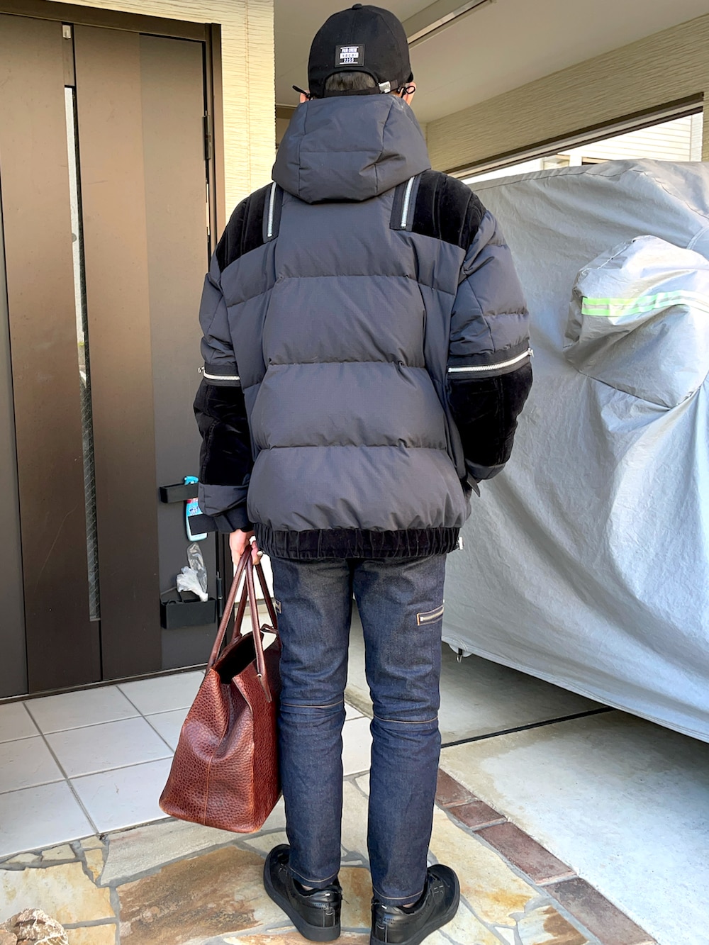 ブラック系のダウンジャケット/コート、ブラウン系のトートバッグ、ブルー系のデニムパンツを着用したメンズの冬コーディネートの2枚目の写真