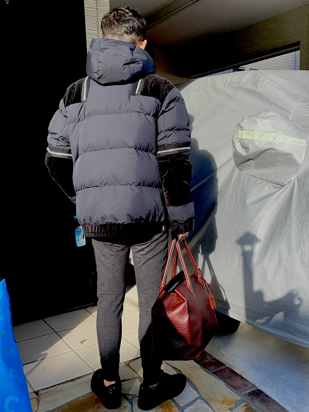 ブラウン系のトートバッグ、ブラック系のダウンジャケット/コート、ブルー系のスウェットを着用したメンズの冬コーディネートの2枚目の写真