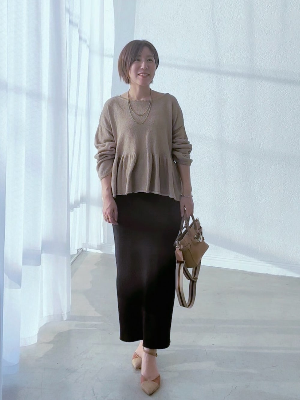 ブラック系のスカート、ブラウン系のパンプス、ベージュ系のトートバッグを着用したレディースの春コーディネートの2枚目の写真