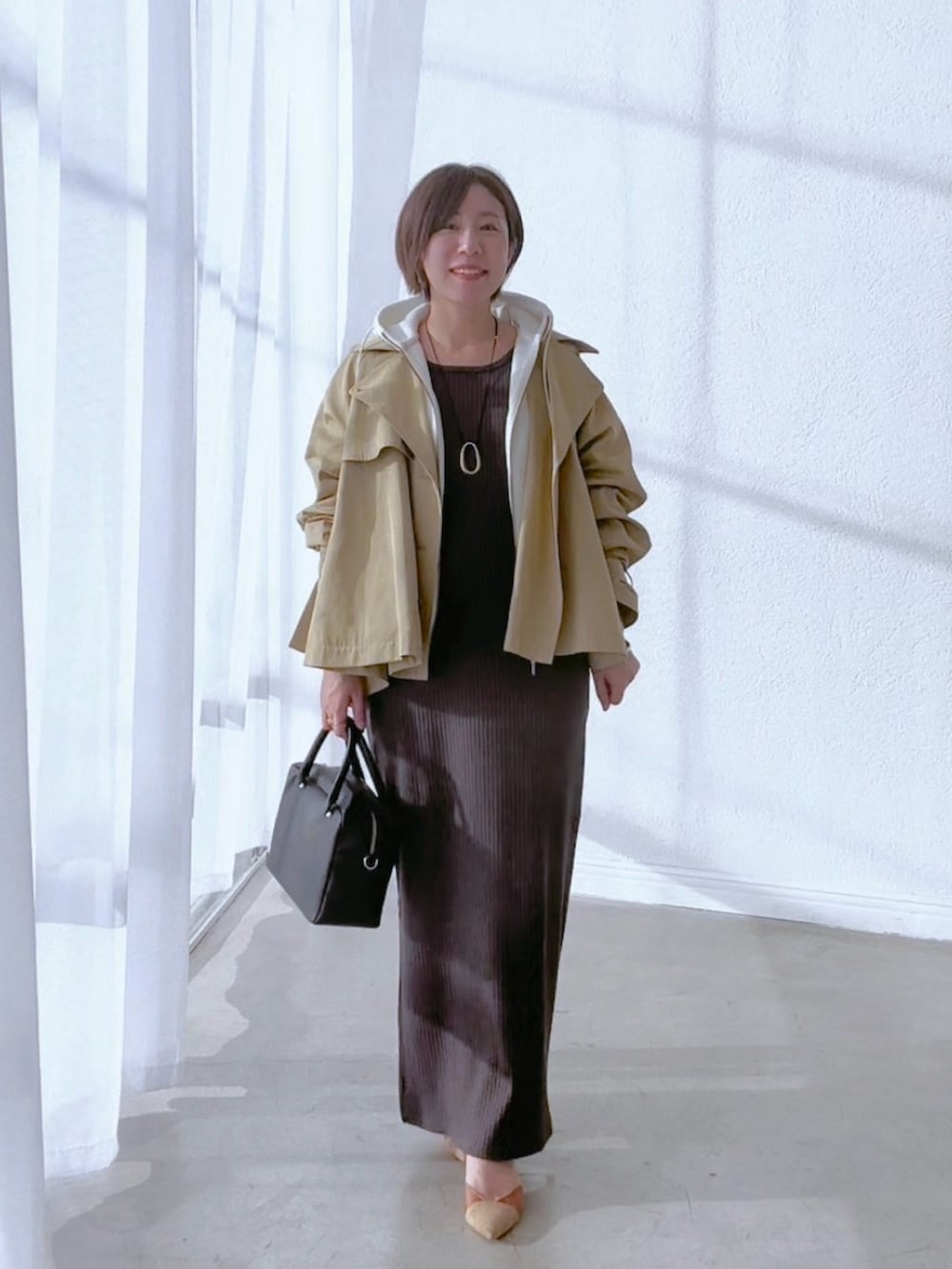 ベージュ系のトレンチコート、グレー系のワンピース、ホワイト系のパーカーを着用したレディースの冬コーディネートの2枚目の写真