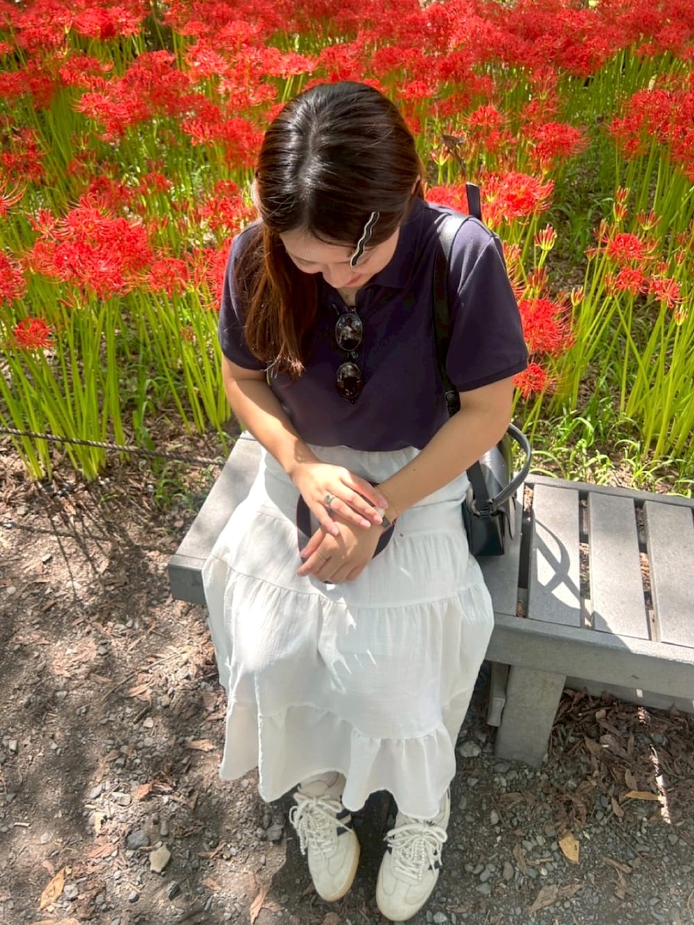 ブルー系のポロシャツ、ホワイト系のスカート、ブラック系のショルダーバッグを着用したレディースの秋コーディネートの2枚目の写真