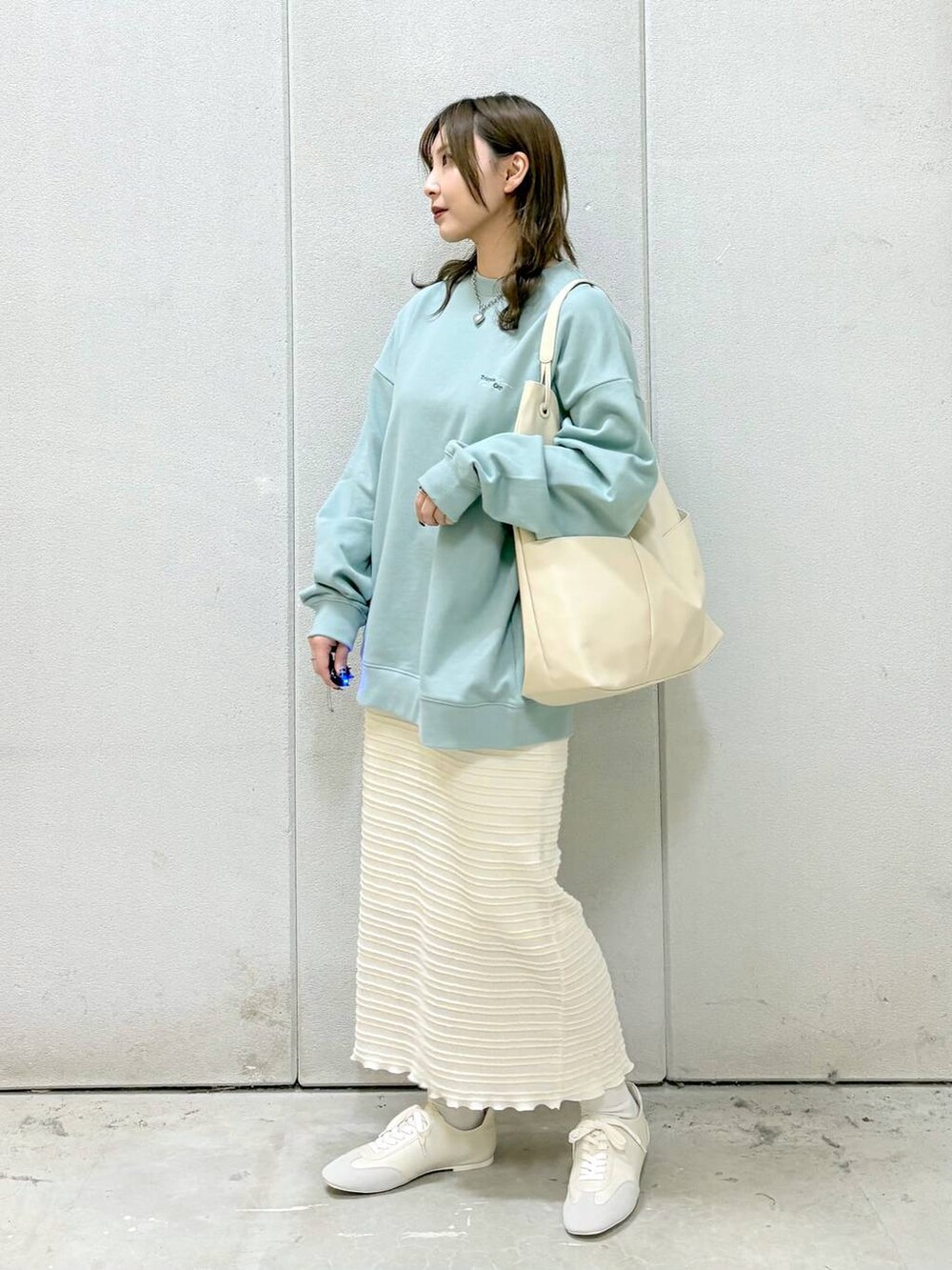 グリーン系のTシャツ/カットソー、ホワイト系のトートバッグ、ホワイト系のスニーカーを着用したレディースの冬コーディネートの2枚目の写真