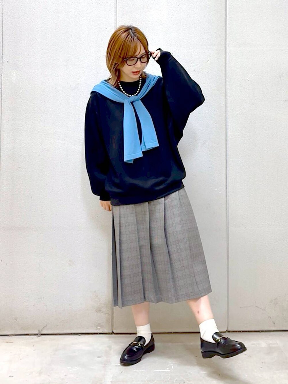 グレー系のスカート、ブラック系のスウェット、ブラック系のローファーを着用したレディースの秋コーディネートの2枚目の写真