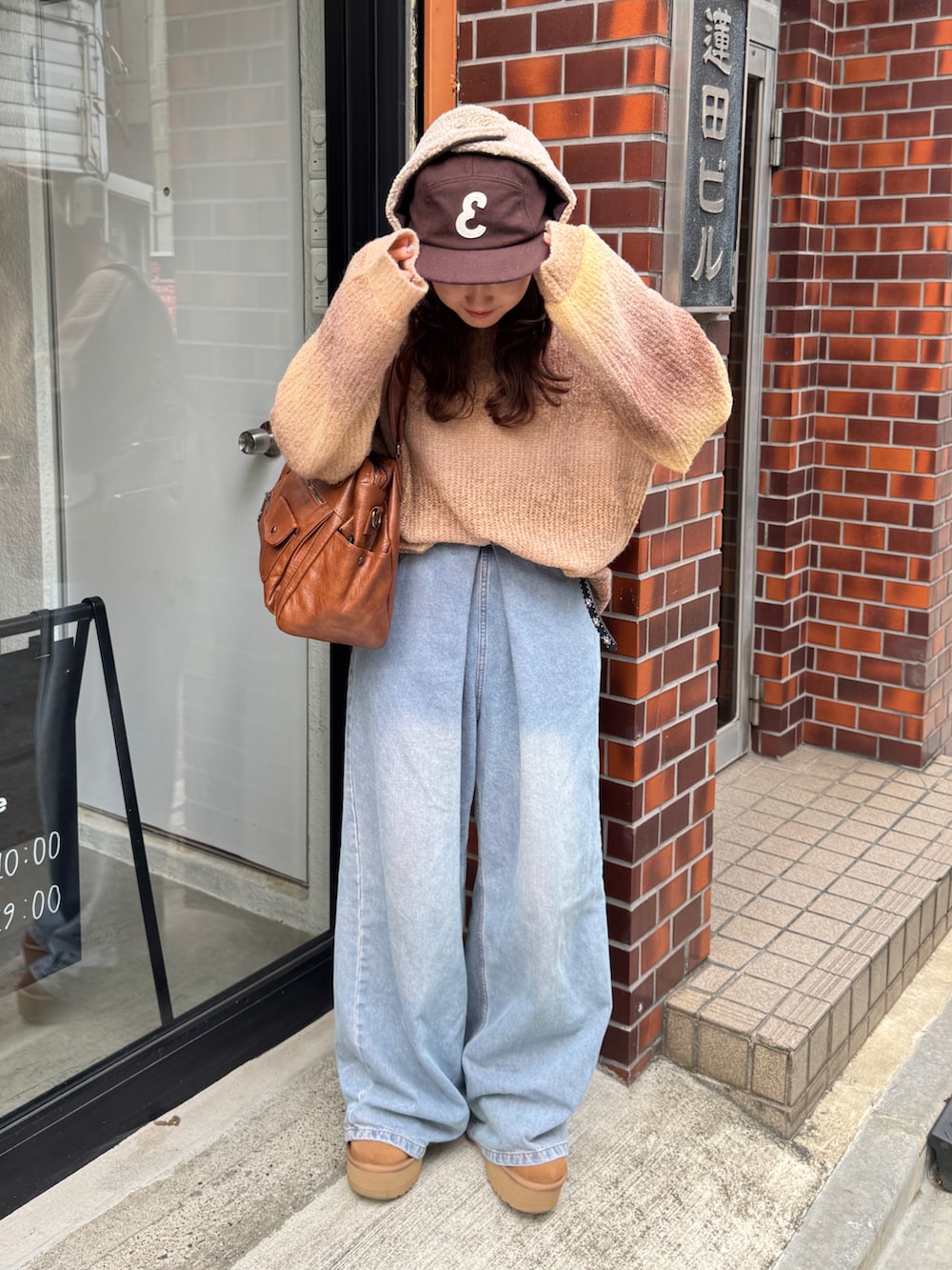 ブルー系のデニムパンツ、ブラウン系のショルダーバッグ、ブラウン系のブーツを着用したレディースの秋コーディネートの2枚目の写真