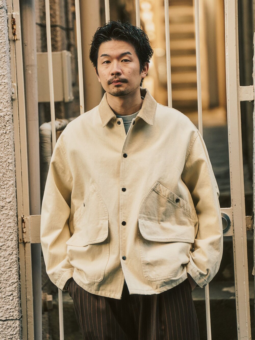 グレー系のニット/セーター、ベージュ系のその他アウター、ブラウン系のスラックスを着用したメンズの冬コーディネートの2枚目の写真