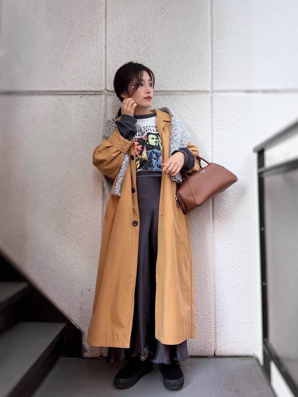 グレー系のスカート、イエロー系のステンカラーコート、ブラウン系のボストンバッグを着用したレディースの冬コーディネートの2枚目の写真