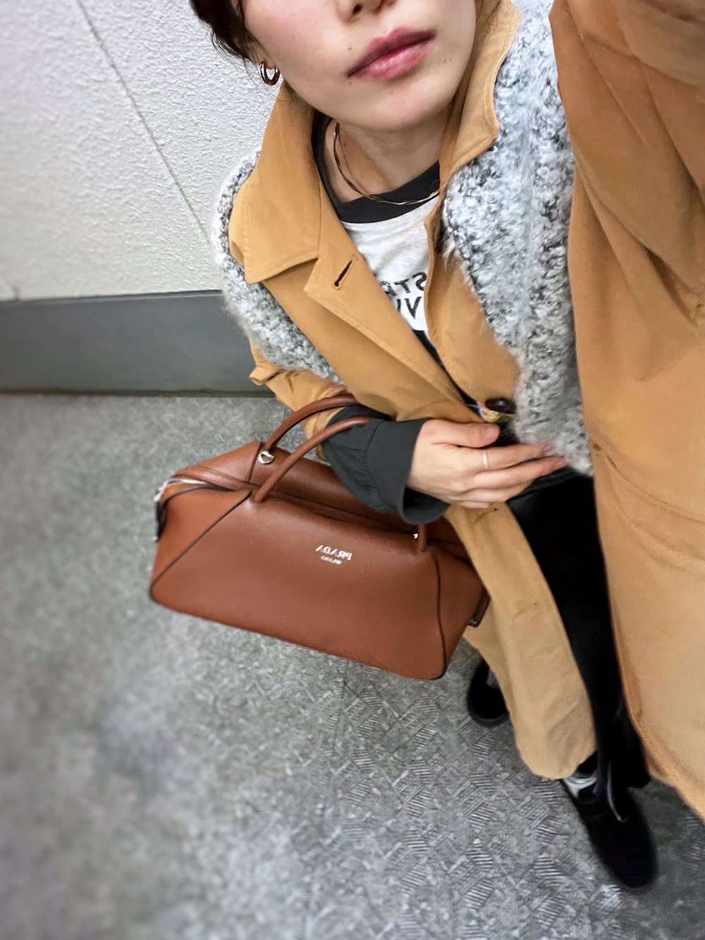 グレー系のスカート、イエロー系のステンカラーコート、ブラウン系のボストンバッグを着用したレディースの冬コーディネートの3枚目の写真