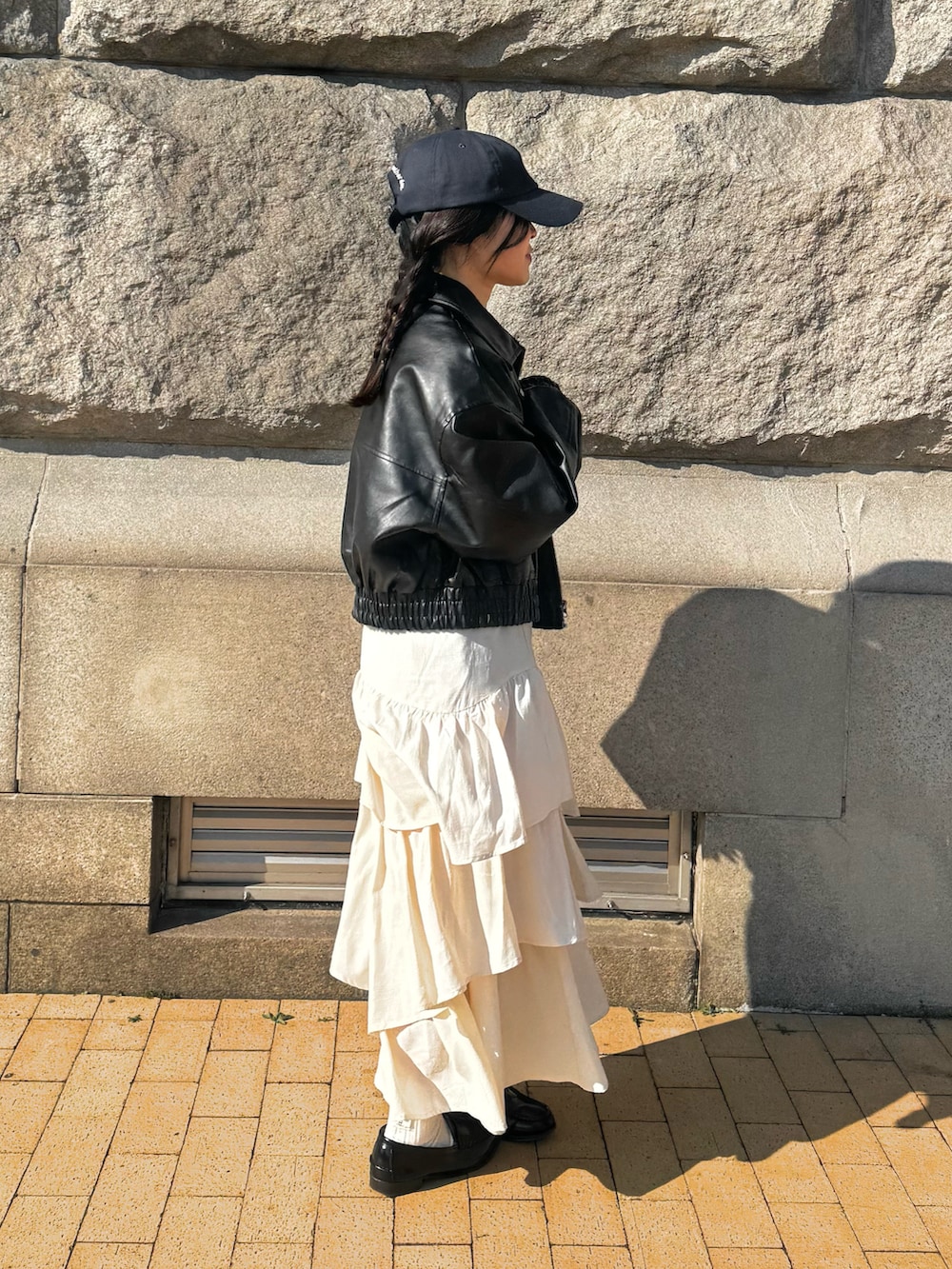 ホワイト系のスカート、ブラック系のブルゾン、ブラック系のローファーを着用したレディースの春コーディネートの2枚目の写真
