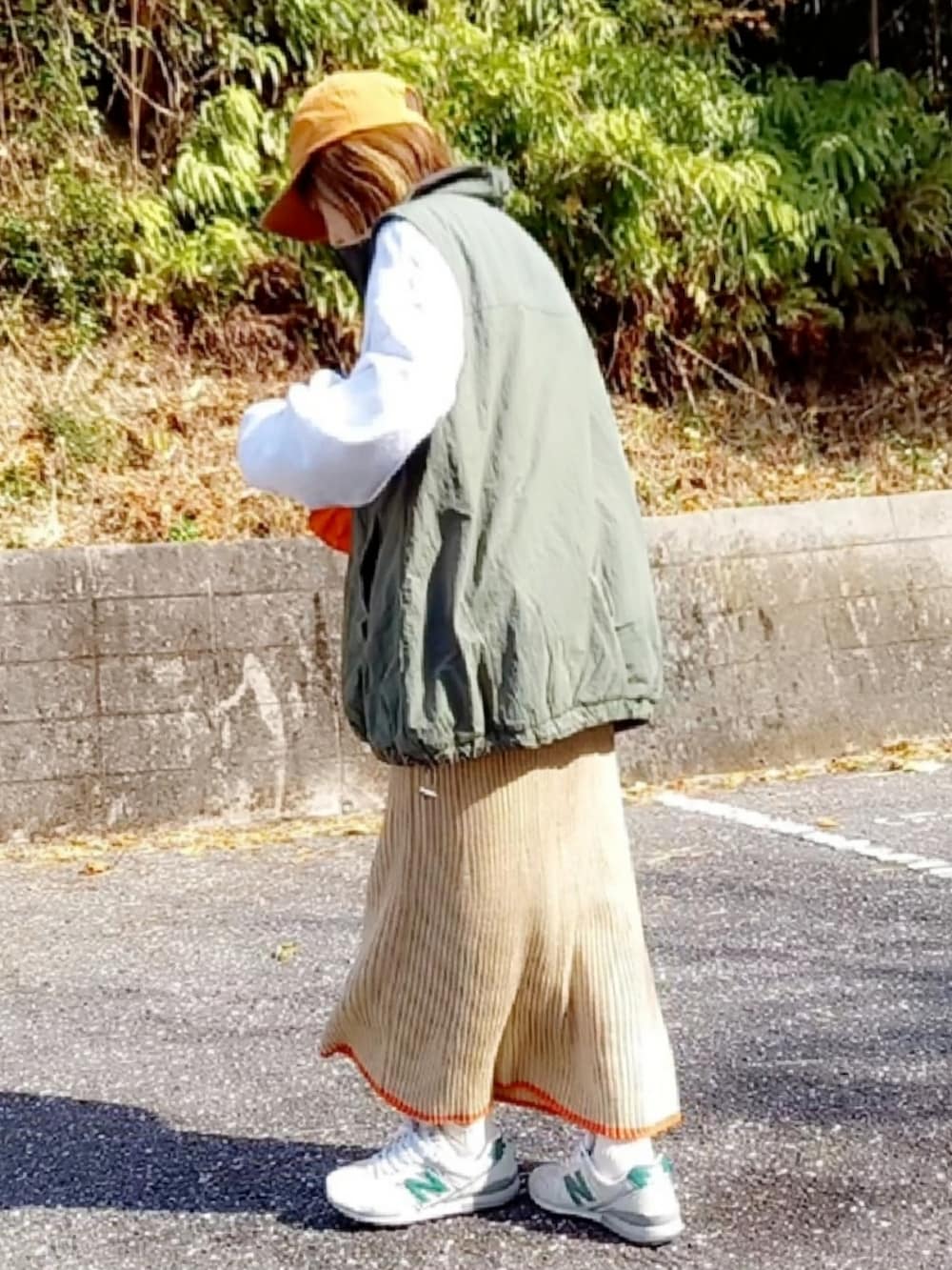 グリーン系のベスト、グレー系のスウェット、オレンジ系のショルダーバッグを着用したレディースの冬コーディネートの2枚目の写真