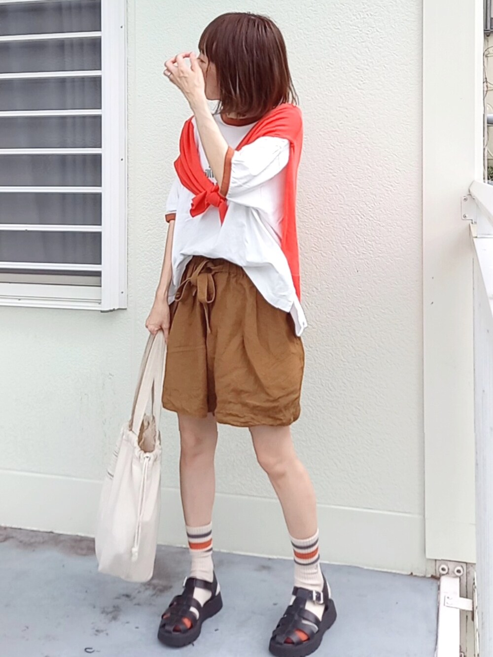 ブラウン系のパンツ、ブラウン系のTシャツ/カットソー、オレンジ系のカーディガン/ボレロを着用したレディースの夏コーディネートの2枚目の写真