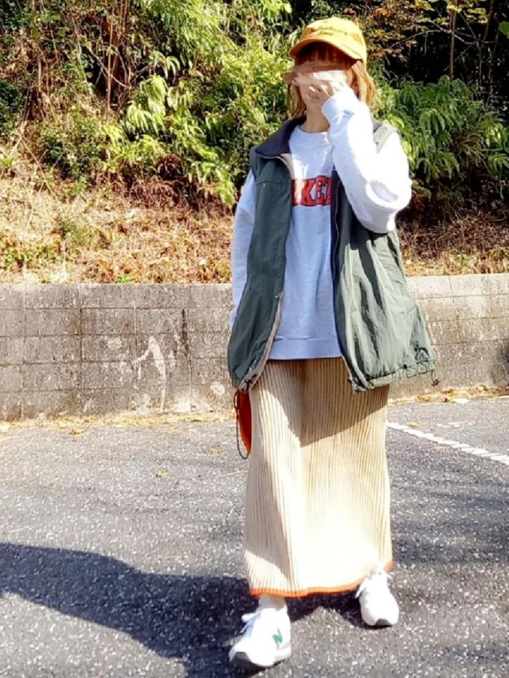 グリーン系のベスト、グレー系のスウェット、オレンジ系のショルダーバッグを着用したレディースの冬コーディネートの3枚目の写真