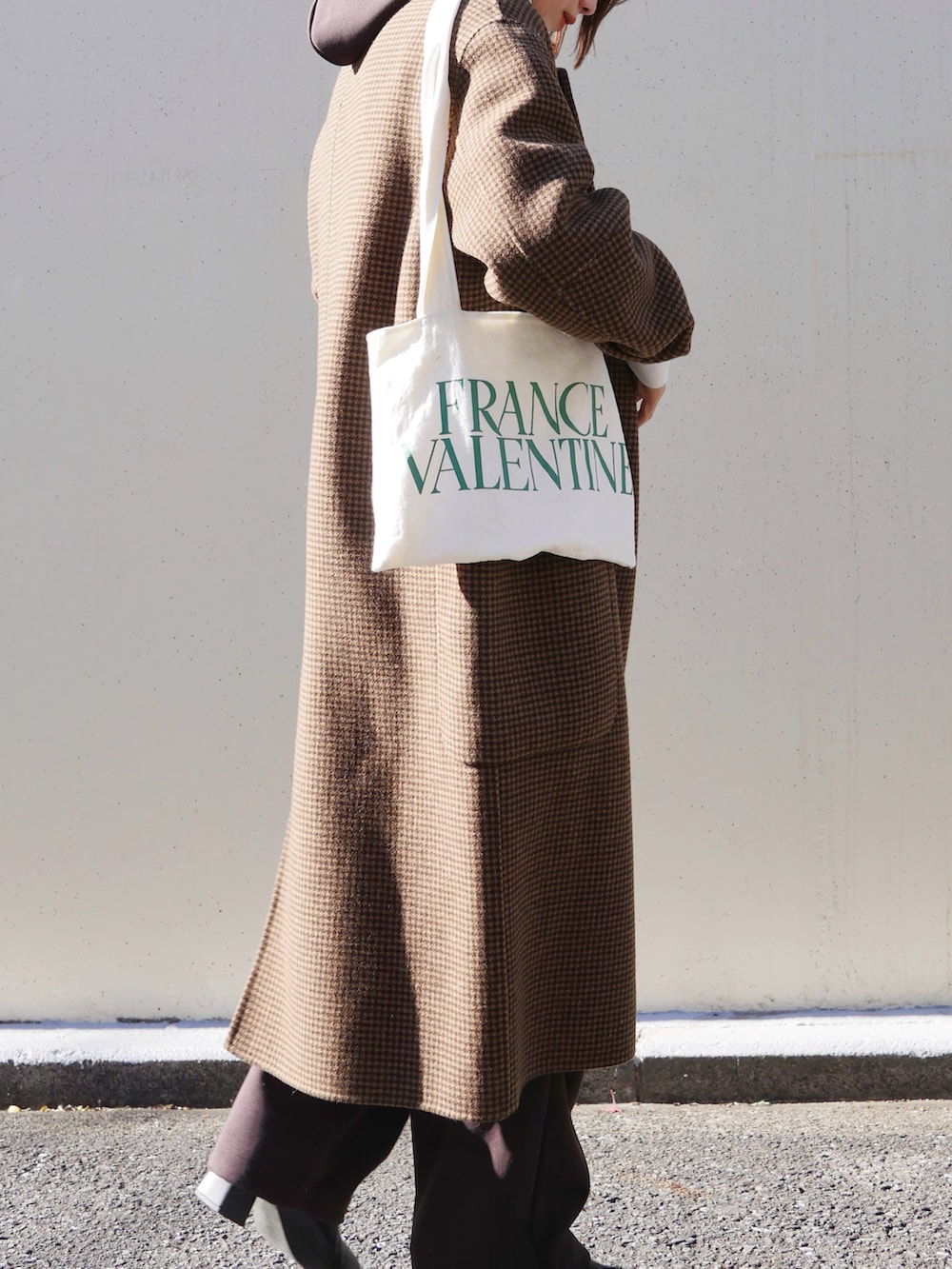 ホワイト系のトートバッグ、ホワイト系のTシャツ/カットソー、ブラウン系のチェスターコートを着用したレディースの冬コーディネートの2枚目の写真