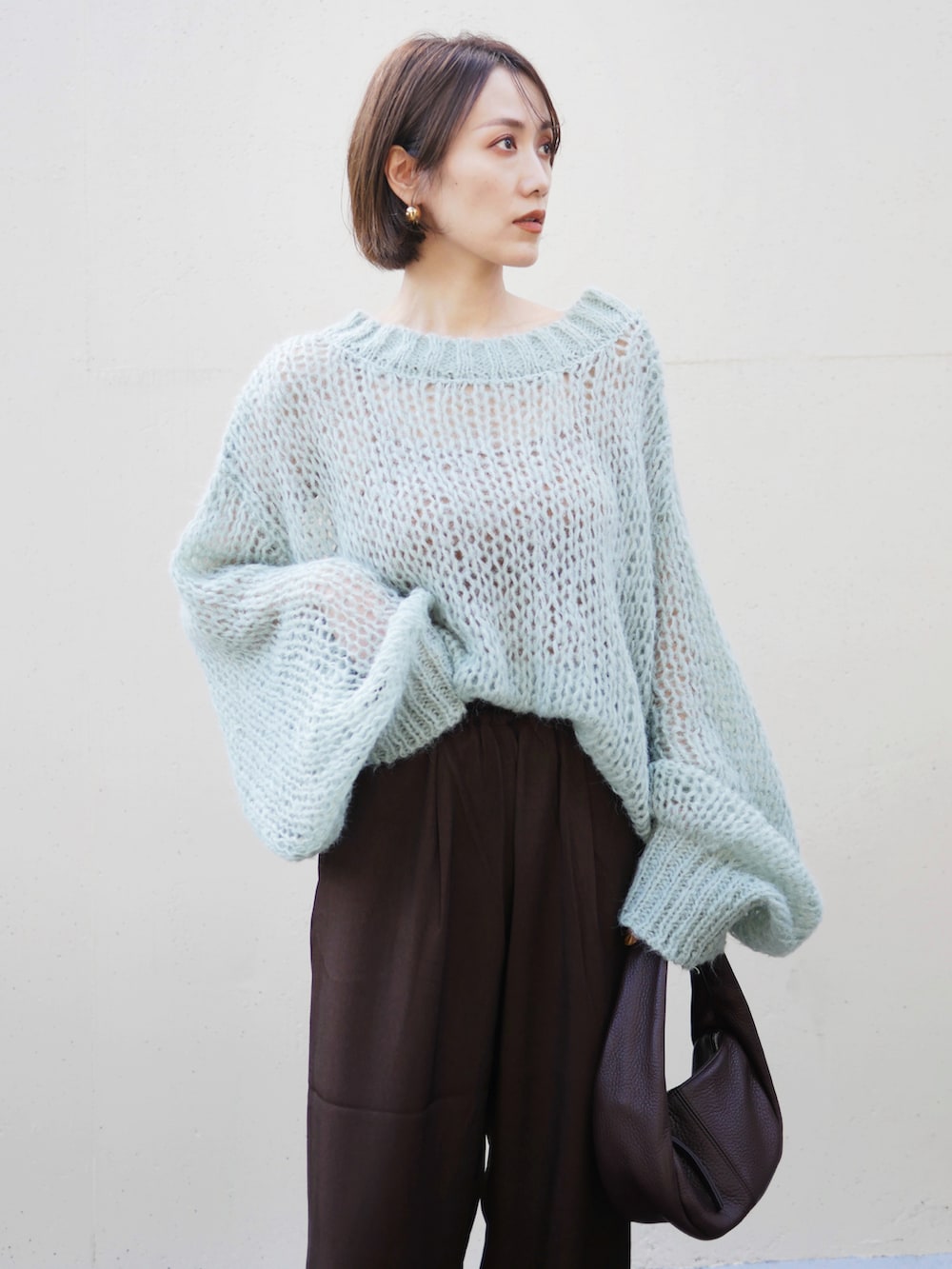 グリーン系のニット/セーター、ブラウン系のスラックス、レッド系のハンドバッグを着用したレディースの秋コーディネートの4枚目の写真