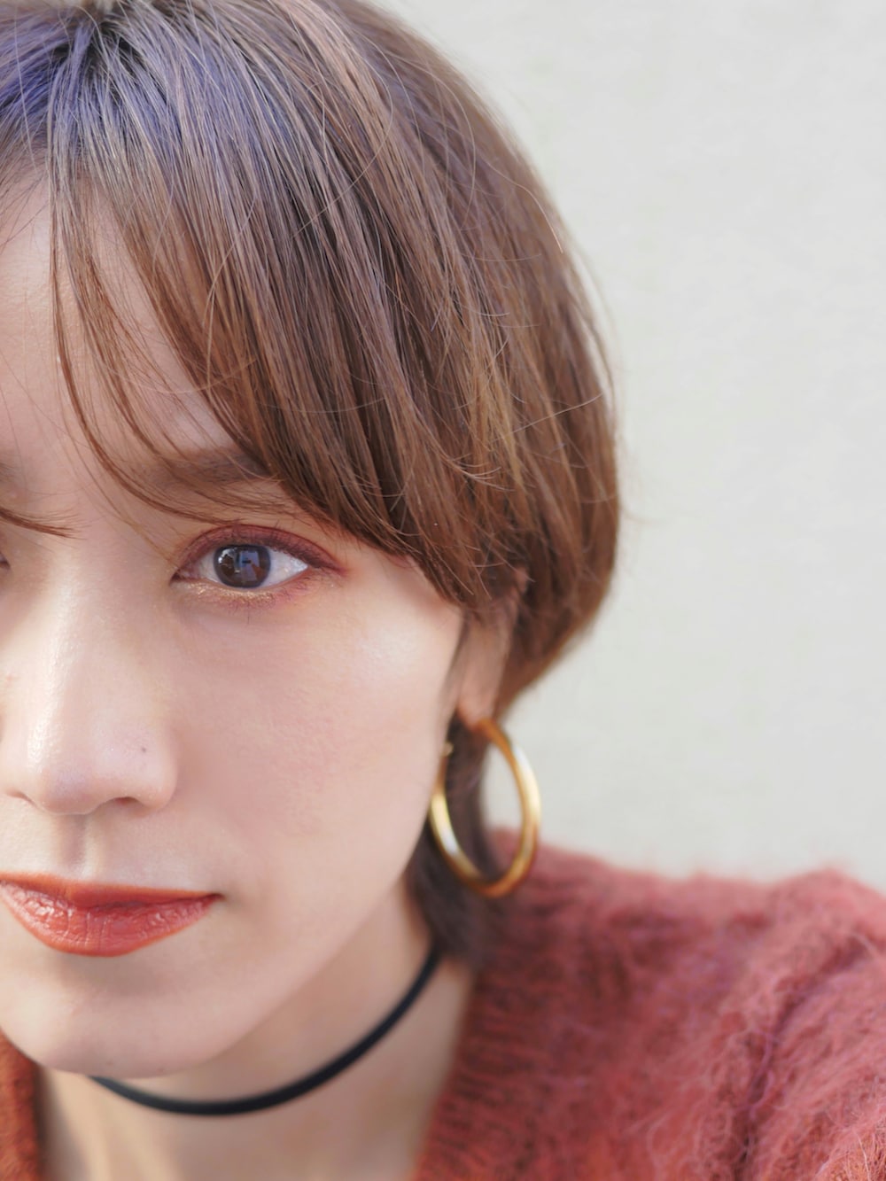 オレンジ系のカーディガン/ボレロ、ブラウン系のライダースジャケット、ブルー系のデニムパンツを着用したレディースの冬コーディネートの2枚目の写真