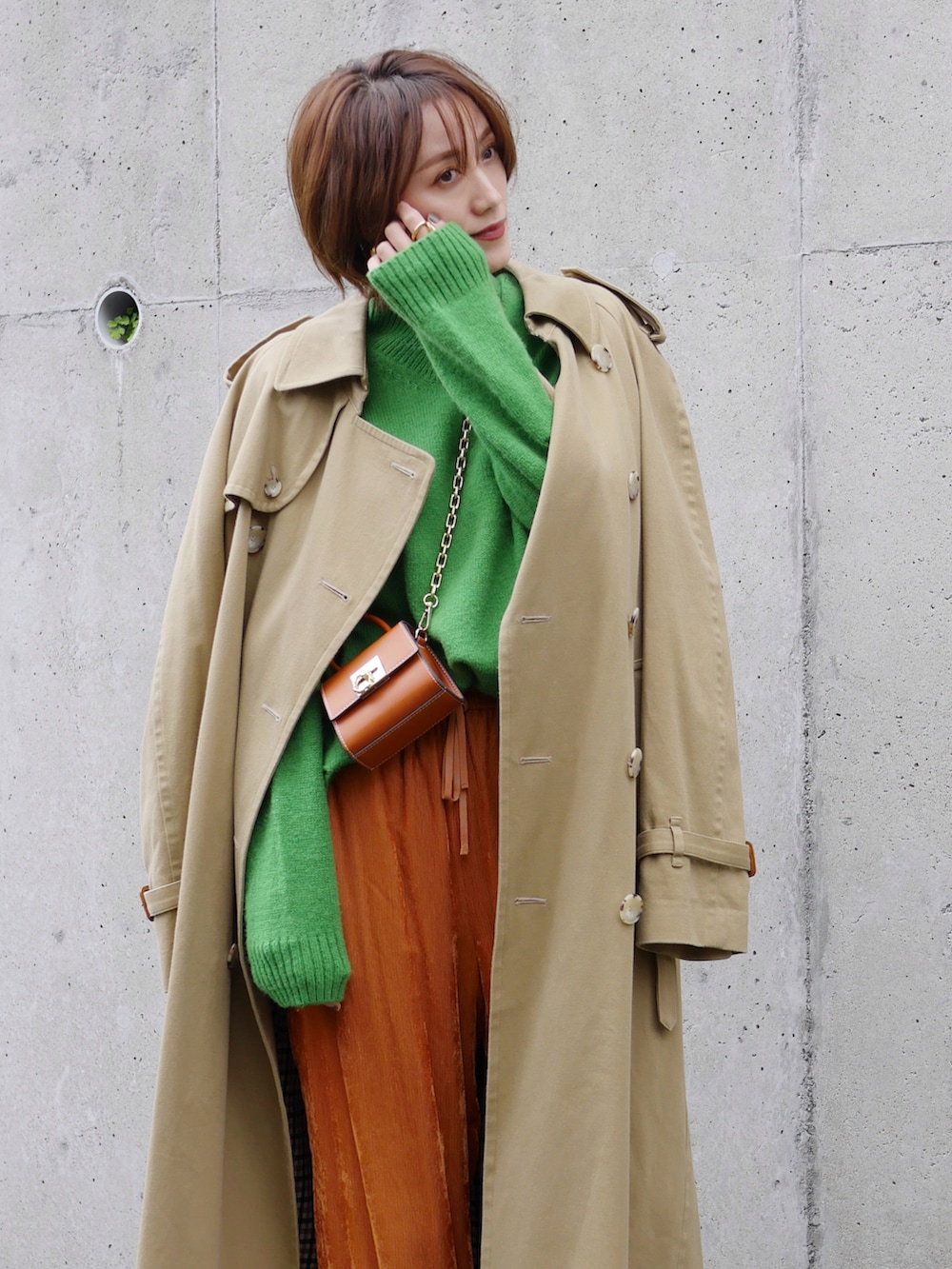 グリーン系のニット/セーター、オレンジ系のその他パンツ、ベージュ系のトレンチコートを着用したレディースの冬コーディネートの2枚目の写真