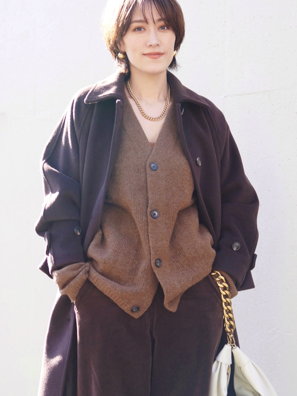 ブラウン系のステンカラーコート、ホワイト系のショルダーバッグ、ブラウン系のカーディガン/ボレロを着用したレディースの冬コーディネートの2枚目の写真