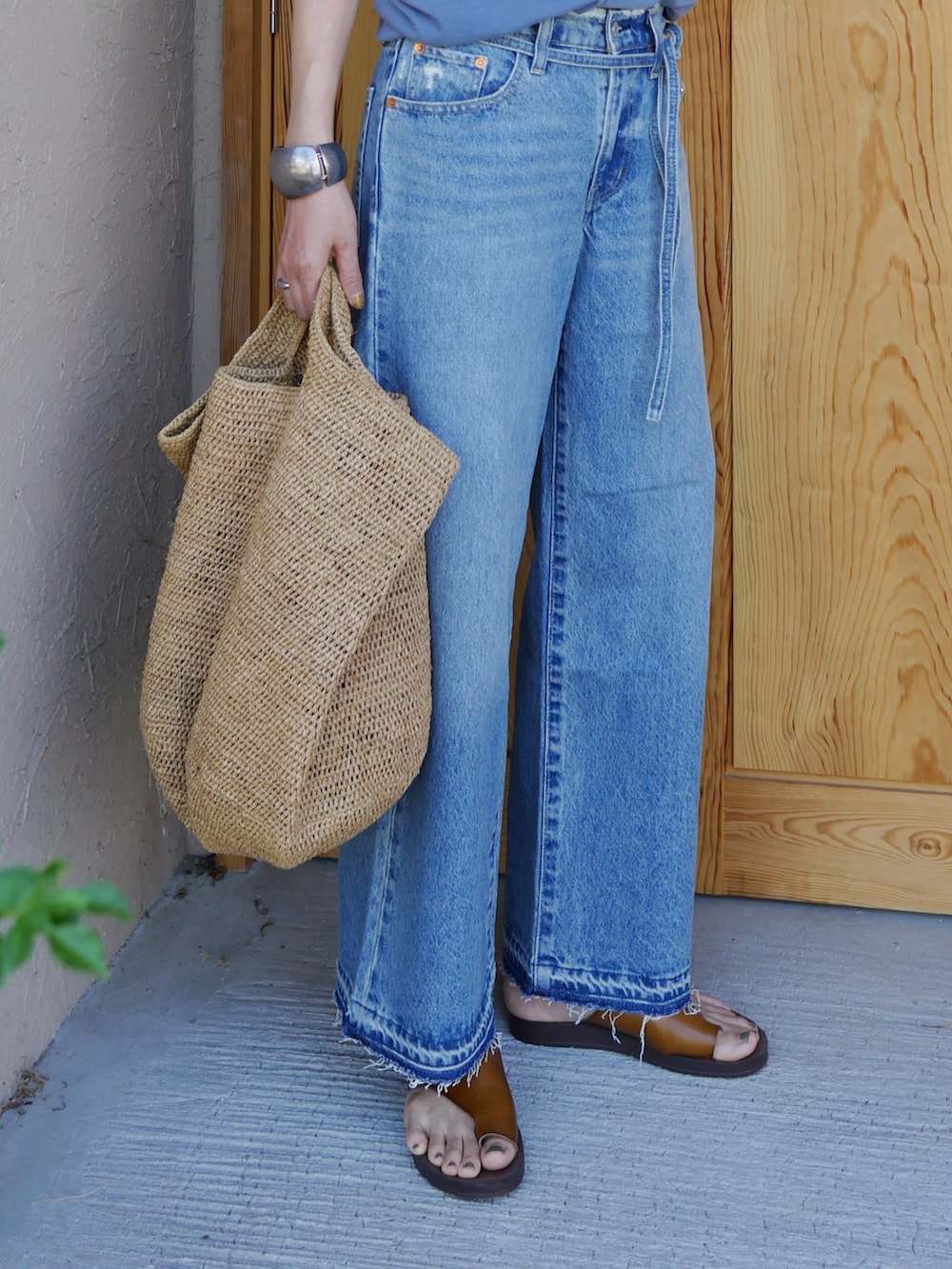 ブルー系のタンクトップ、ブルー系のデニムパンツ、ブラウン系のかごバッグを着用したレディースの夏コーディネートの2枚目の写真