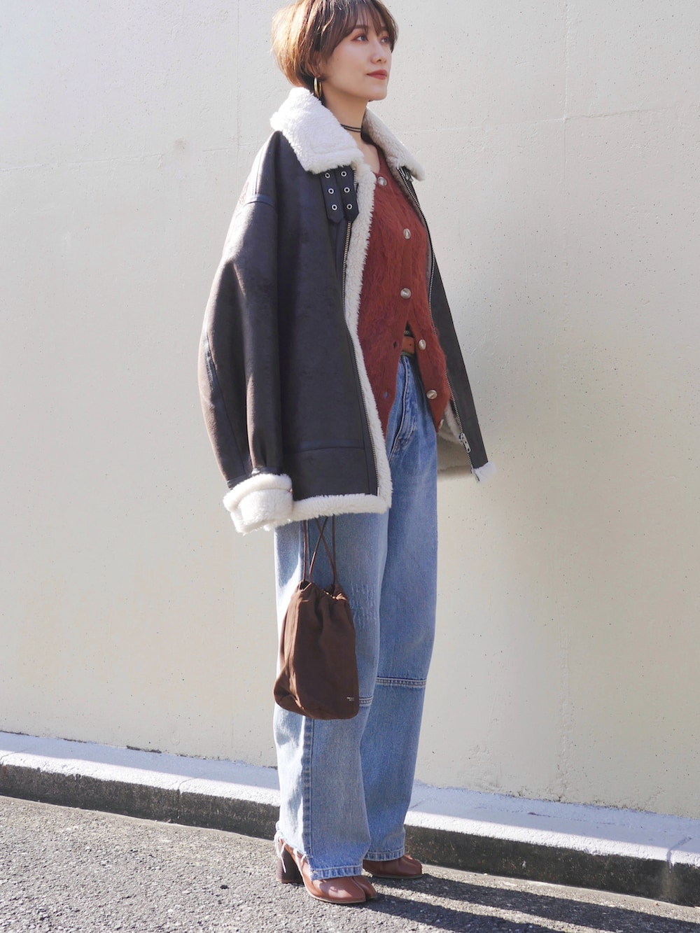 オレンジ系のカーディガン/ボレロ、ブラウン系のライダースジャケット、ブルー系のデニムパンツを着用したレディースの冬コーディネートの4枚目の写真