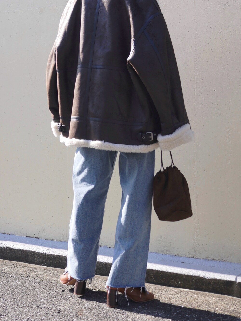 オレンジ系のカーディガン/ボレロ、ブラウン系のライダースジャケット、ブルー系のデニムパンツを着用したレディースの冬コーディネートの5枚目の写真