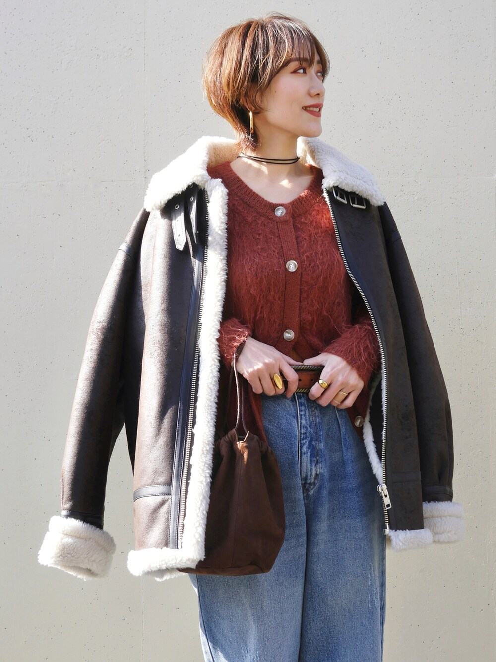 オレンジ系のカーディガン/ボレロ、ブラウン系のライダースジャケット、ブルー系のデニムパンツを着用したレディースの冬コーディネートの3枚目の写真