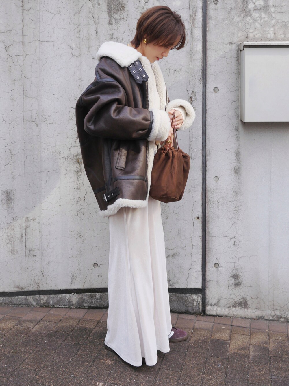 ブラウン系のライダースジャケット、ホワイト系のスカート、ブラウン系のスニーカーを着用したレディースの冬コーディネートの3枚目の写真