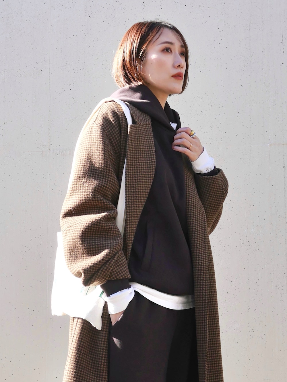 ホワイト系のトートバッグ、ホワイト系のTシャツ/カットソー、ブラウン系のチェスターコートを着用したレディースの冬コーディネートの3枚目の写真