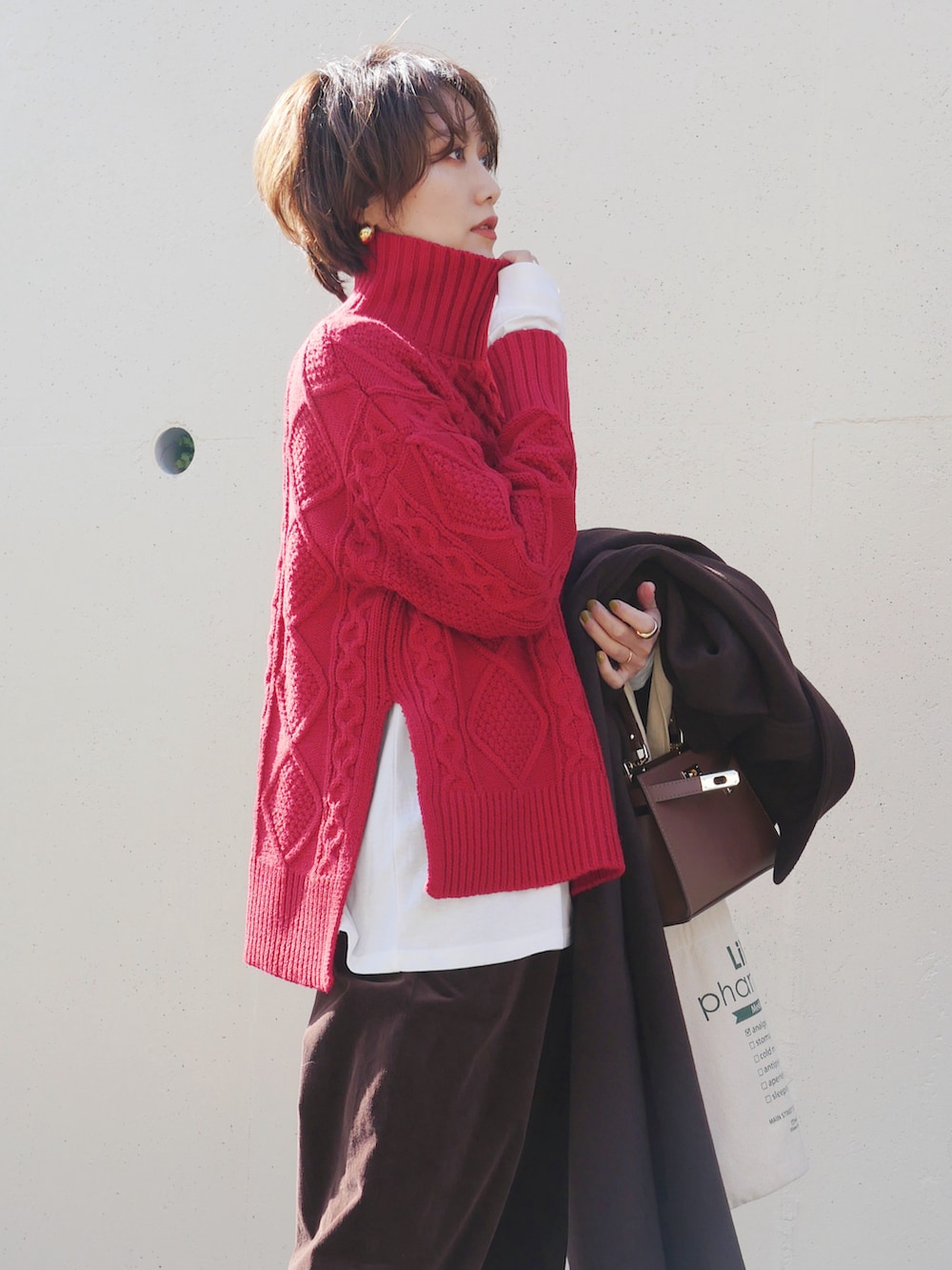 レッド系のニット/セーター、ブラウン系のショルダーバッグ、ブラウン系のステンカラーコートを着用したレディースの冬コーディネートの2枚目の写真
