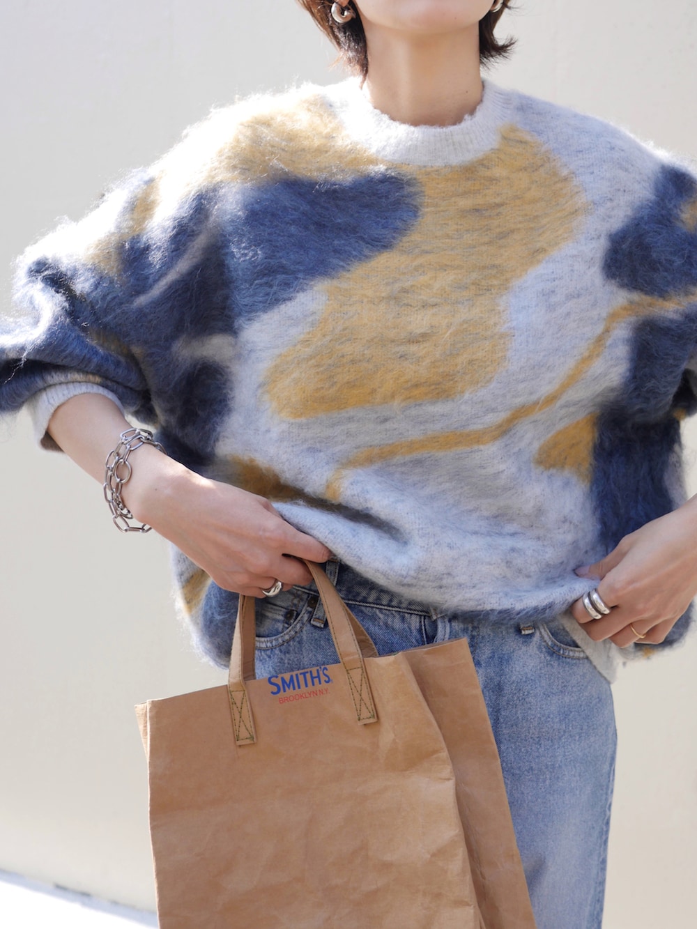 ブルー系のニット/セーター、ベージュ系のトートバッグ、シルバー系のピアス（両耳用）を着用したレディースの秋コーディネートの3枚目の写真