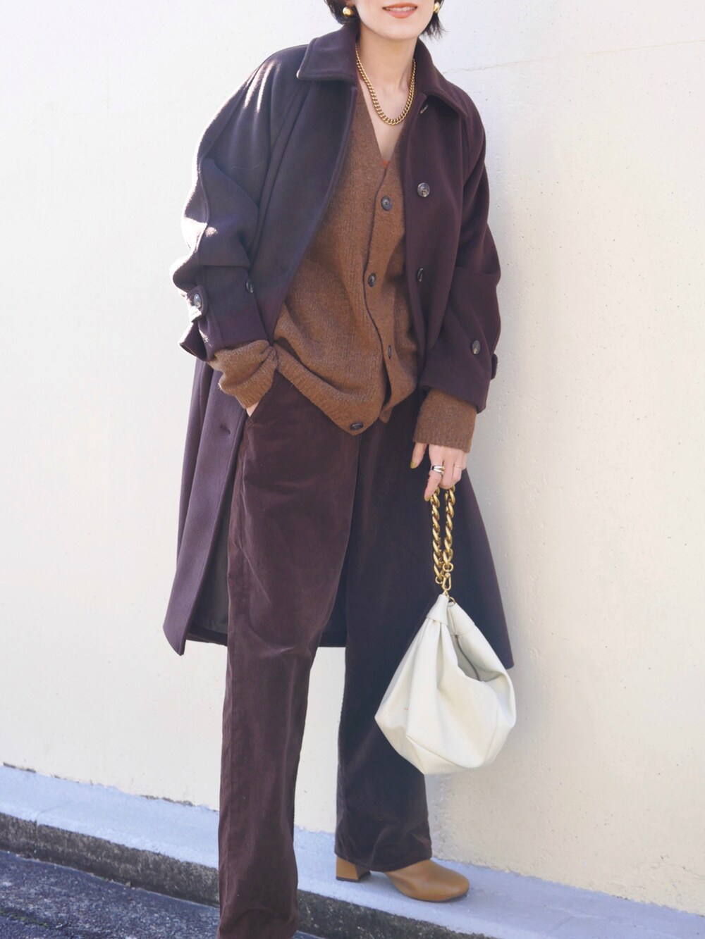 ブラウン系のステンカラーコート、ホワイト系のショルダーバッグ、ブラウン系のカーディガン/ボレロを着用したレディースの冬コーディネートの4枚目の写真