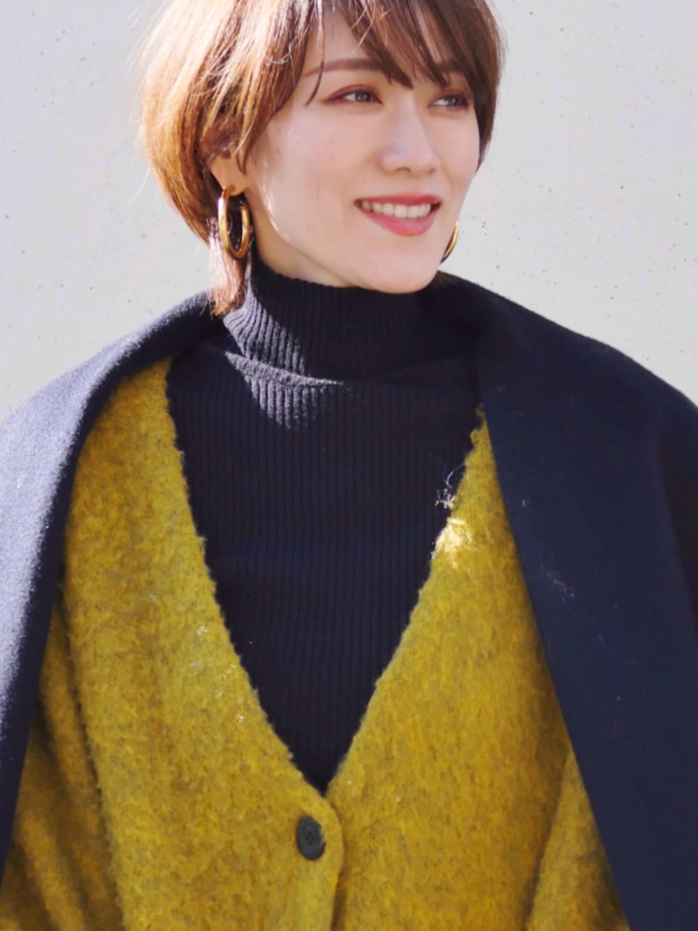 ブラック系のニット/セーター、イエロー系のスカート、ブルー系のカーディガン/ボレロを着用したレディースの冬コーディネートの2枚目の写真