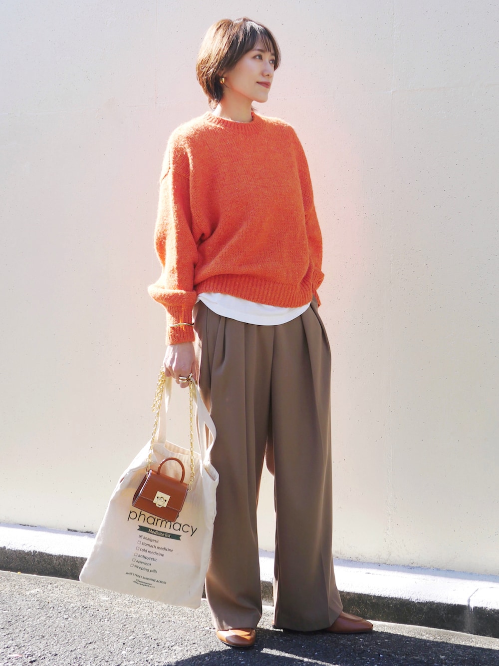 オレンジ系のニット/セーター、ベージュ系のその他パンツ、イエロー系のショルダーバッグを着用したレディースの秋コーディネートの4枚目の写真