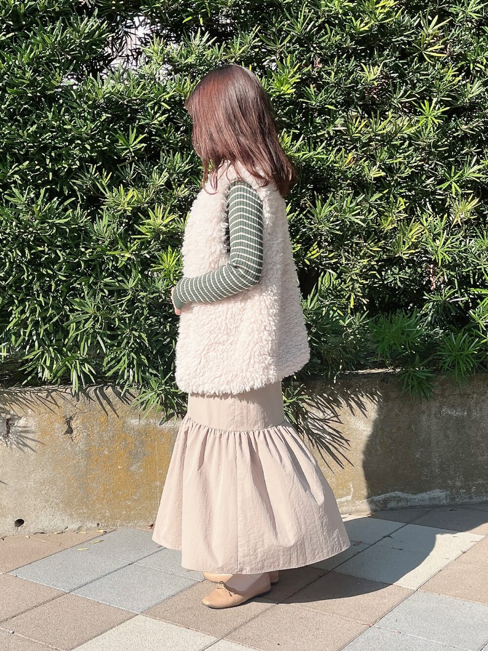 ベージュ系のベスト、グリーン系のニット/セーター、ブラウン系のスカートを着用したレディースの秋コーディネートの2枚目の写真