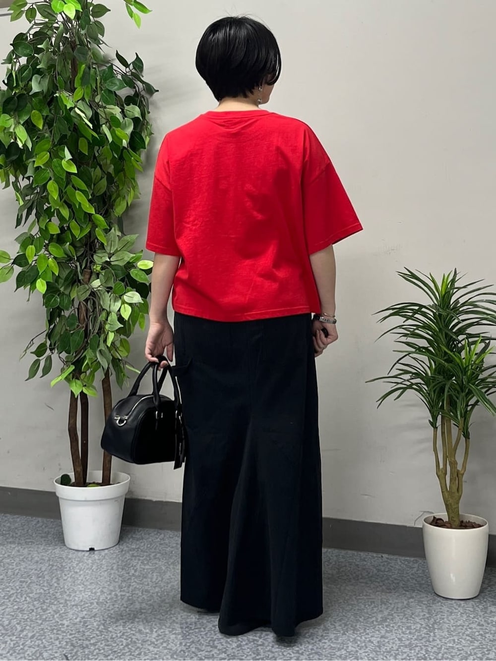 レッド系のTシャツ/カットソー、ブラック系のスカート、ブラック系のショルダーバッグを着用したレディースの春コーディネートの3枚目の写真