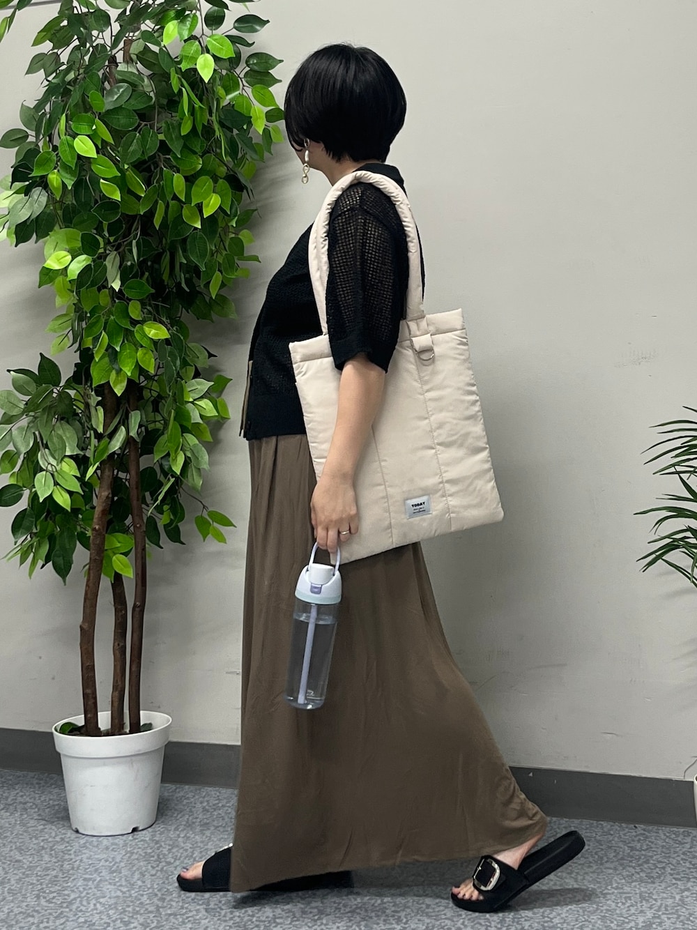 ブラウン系のスカート、ブラック系のニット/セーター、ホワイト系のトートバッグを着用したレディースの春コーディネートの2枚目の写真