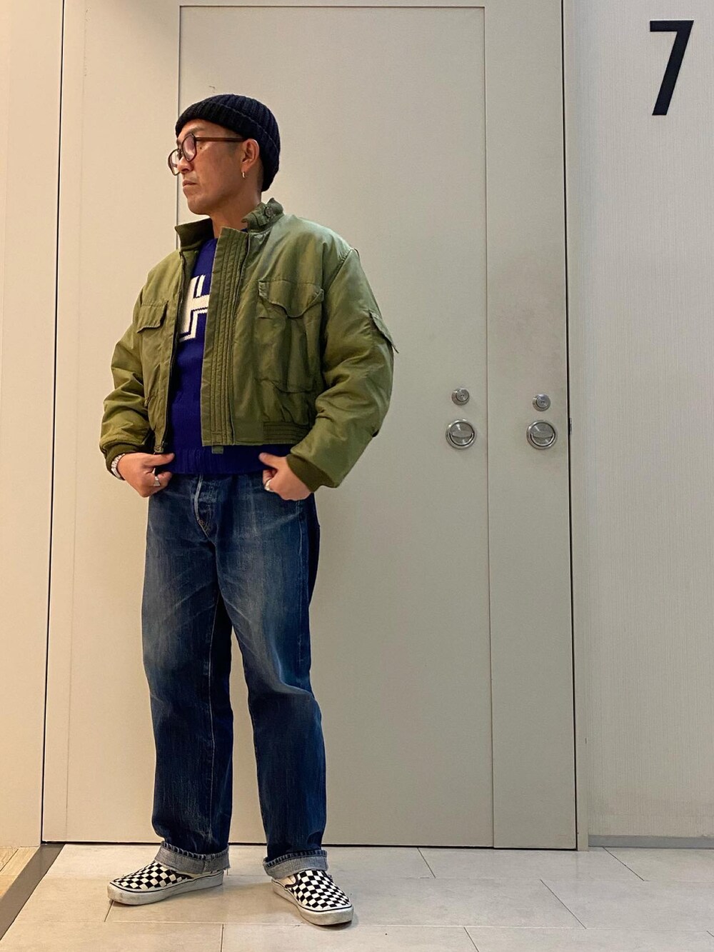 グリーン系のミリタリージャケット、ブルー系のニット/セーター、ブルー系のデニムパンツを着用したメンズの冬コーディネートの2枚目の写真