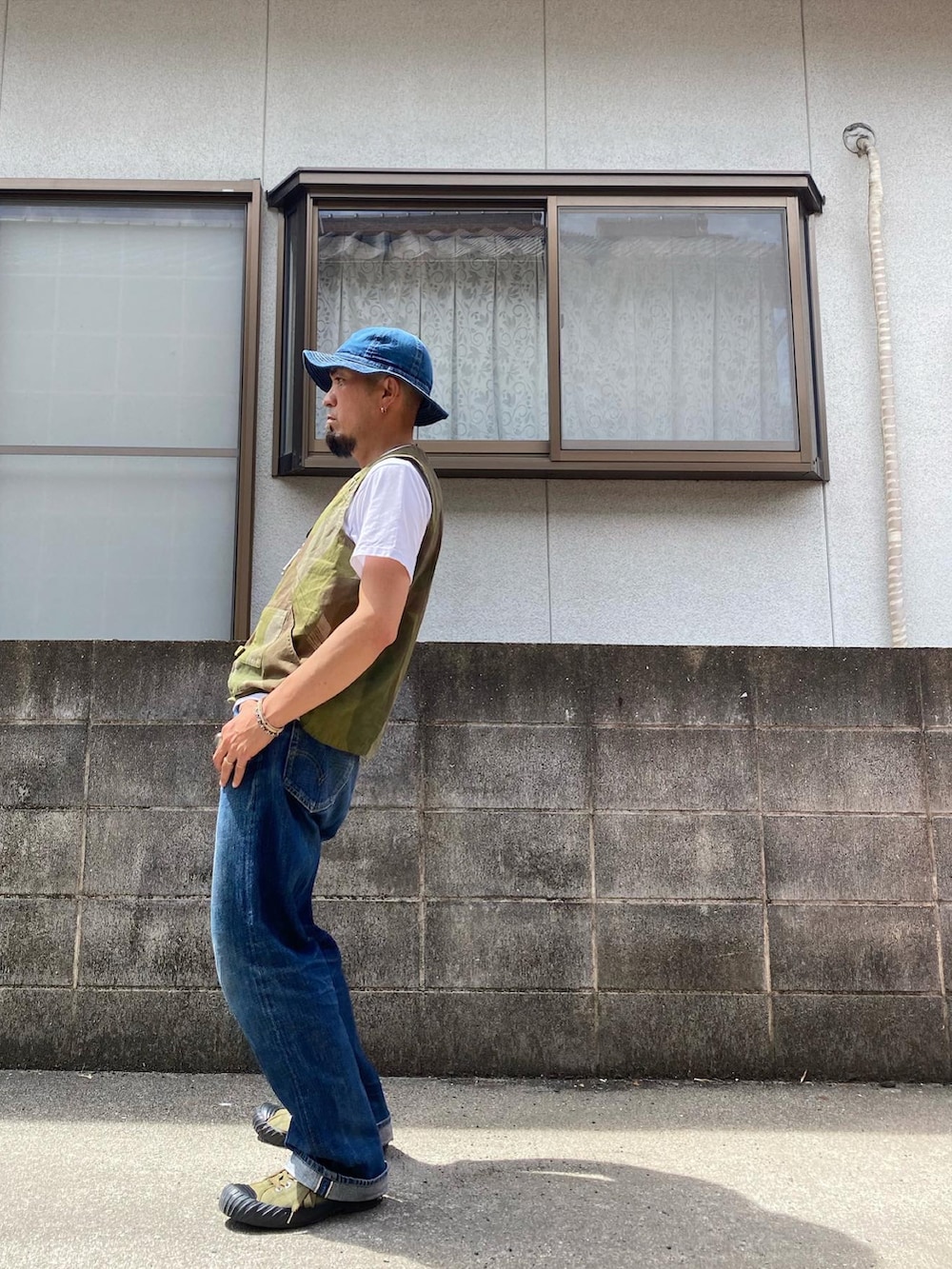 グリーン系のベスト、ブルー系のデニムパンツ、グリーン系のスニーカーを着用したメンズの夏コーディネートの2枚目の写真