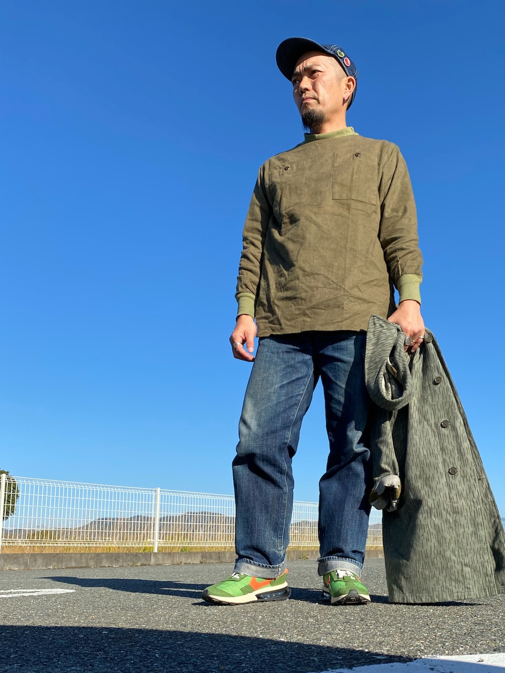 グリーン系のミリタリージャケット、グリーン系のシャツ/ブラウス、ブルー系のデニムパンツを着用したメンズの秋コーディネートの2枚目の写真