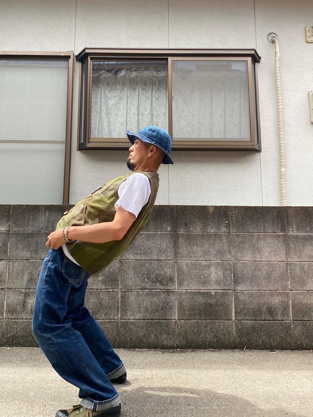 グリーン系のベスト、ブルー系のデニムパンツ、グリーン系のスニーカーを着用したメンズの夏コーディネートの3枚目の写真