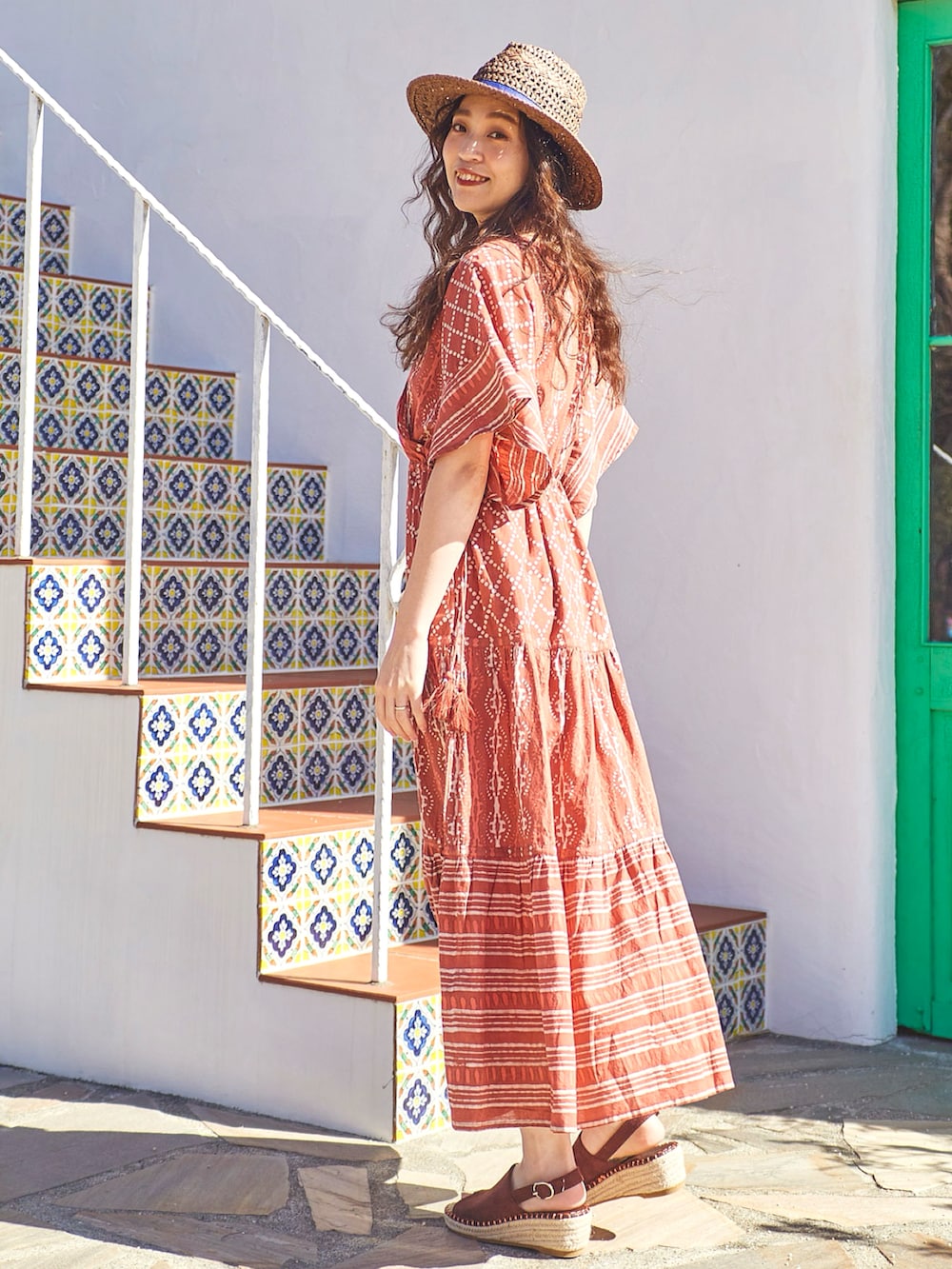 オレンジ系のワンピース、ブラウン系のサンダル、ブラウン系のハットを着用したレディースの夏コーディネートの2枚目の写真