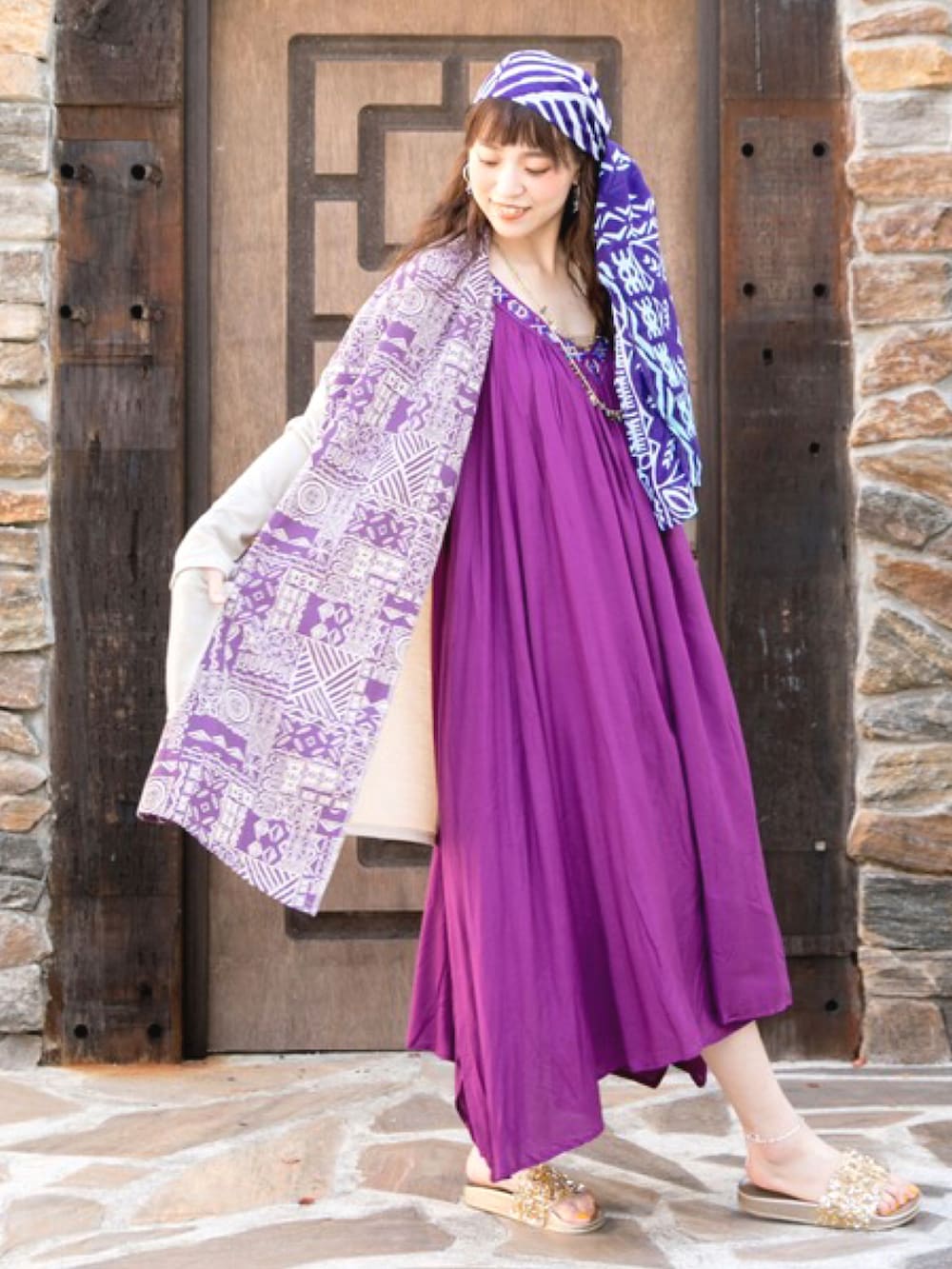 パープル系のワンピース、ゴールド系のサンダル、ベージュ系のカーディガン/ボレロを着用したレディースの夏コーディネートの2枚目の写真