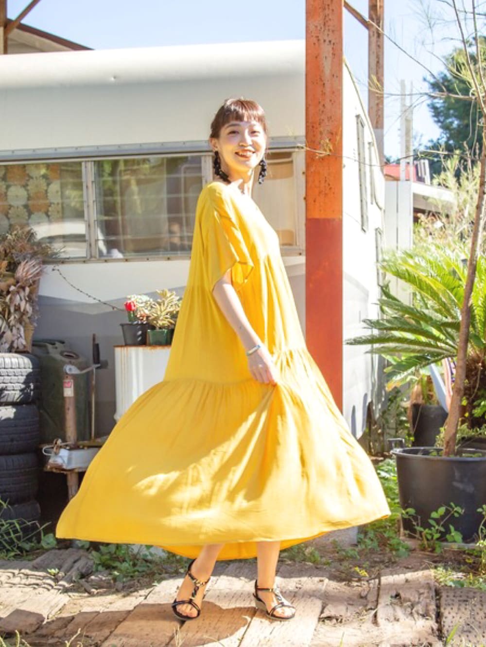 イエロー系のワンピース、ブラック系のサンダル、ブラック系のピアス（両耳用）を着用したレディースの春コーディネートの4枚目の写真