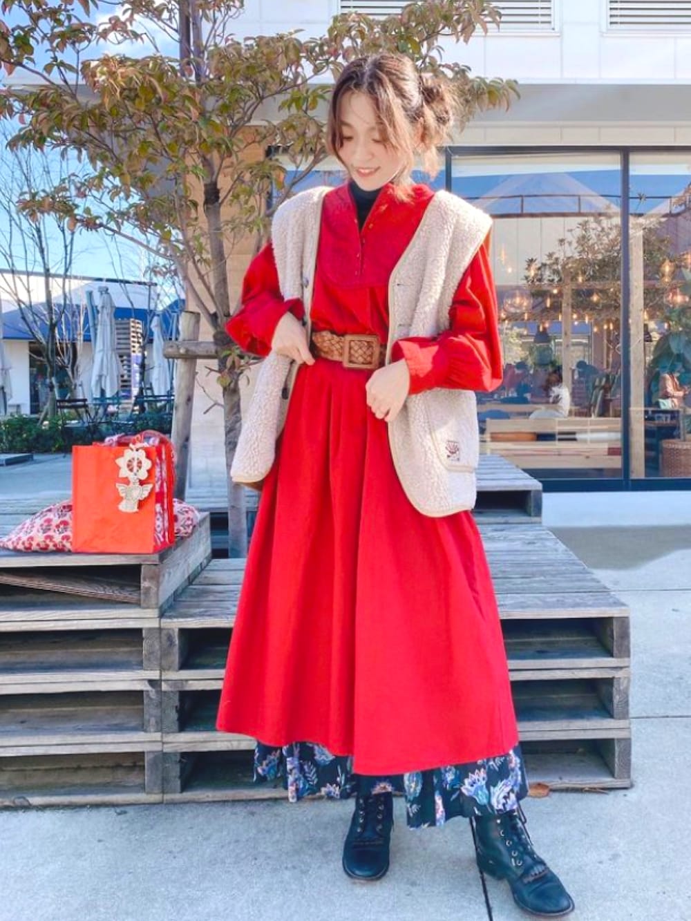 レッド系のワンピース、ベージュ系のベスト、ブラック系のスカートを着用したレディースの冬コーディネートの2枚目の写真