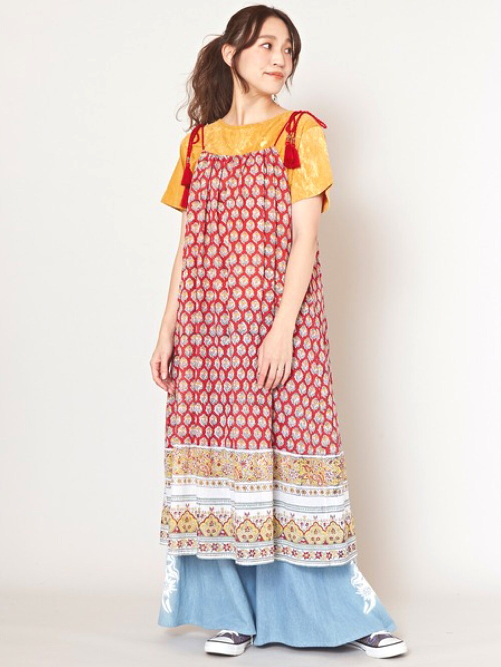 レッド系のワンピース、ブルー系のデニムパンツ、ブラック系のスニーカーを着用したレディースの春コーディネートの2枚目の写真