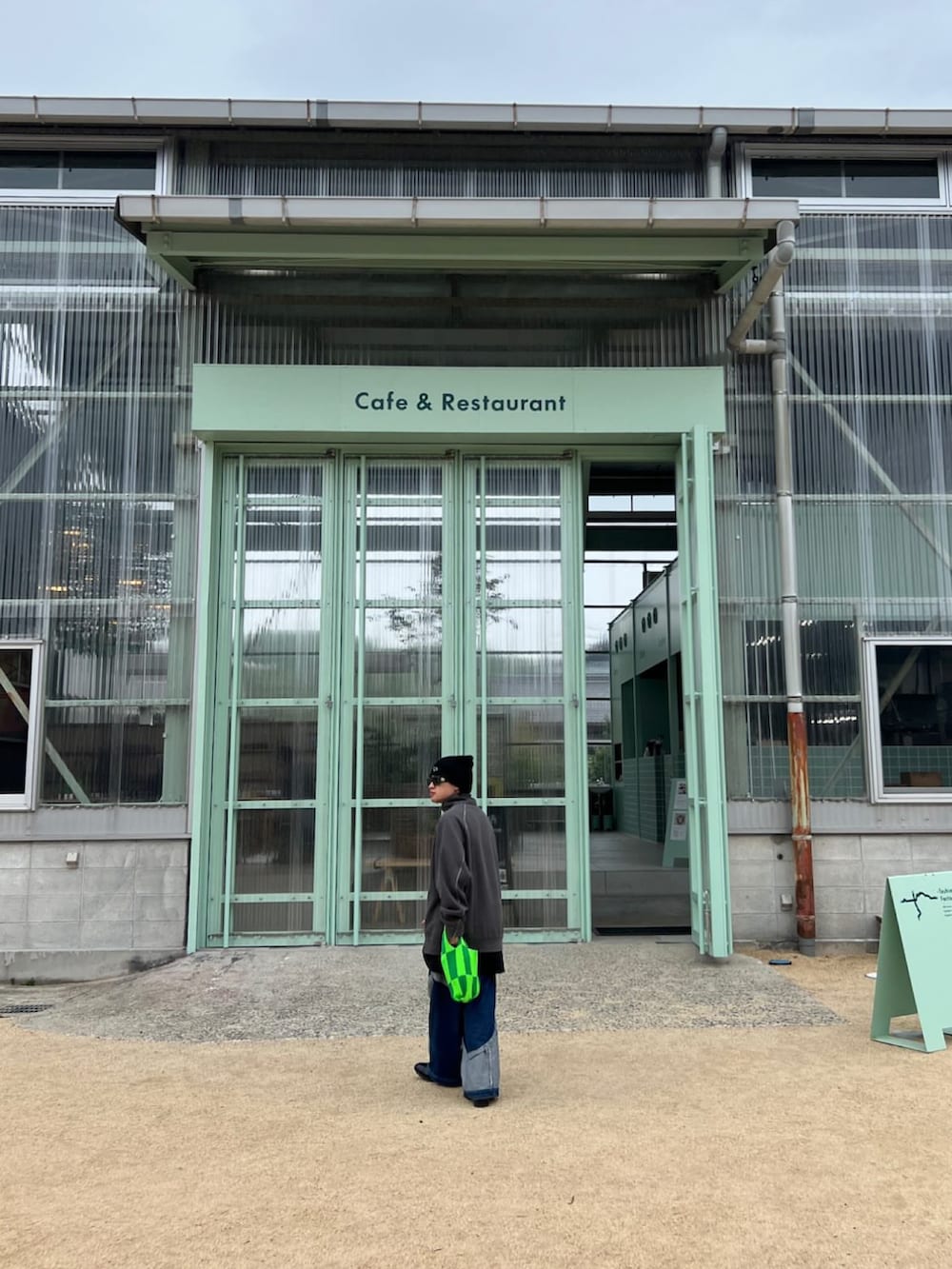 グレー系のスウェット、ブルー系のデニムパンツ、グリーン系のトートバッグを着用したメンズの春コーディネートの2枚目の写真