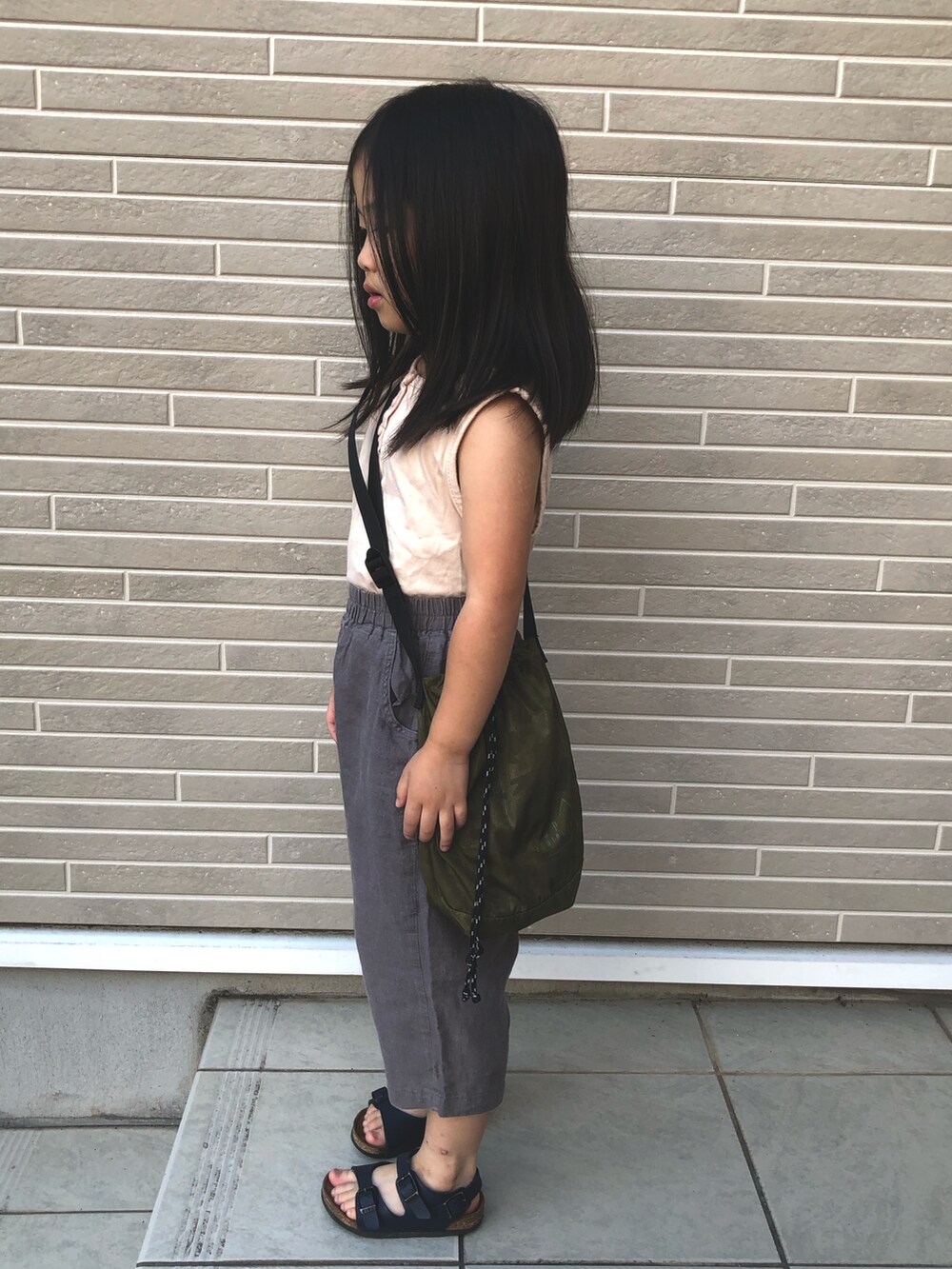 グレー系のパンツ、ベージュ系のタンクトップ、ブルー系のサンダルを着用したキッズの夏コーディネートの2枚目の写真