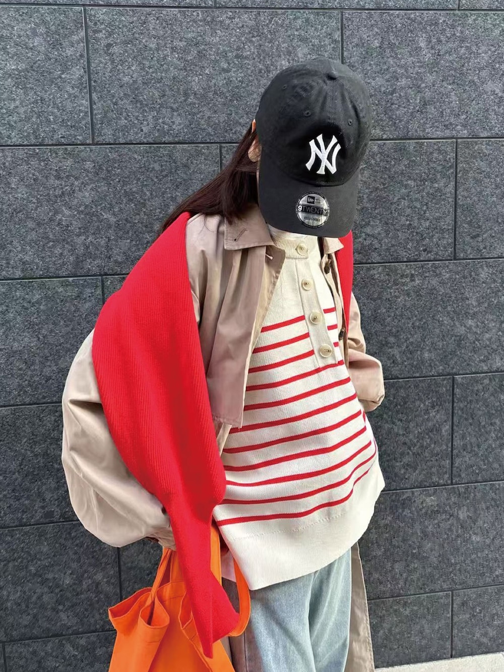 レッド系のニット/セーター、ベージュ系のトレンチコート、ブルー系のデニムパンツを着用したレディースの冬コーディネートの2枚目の写真