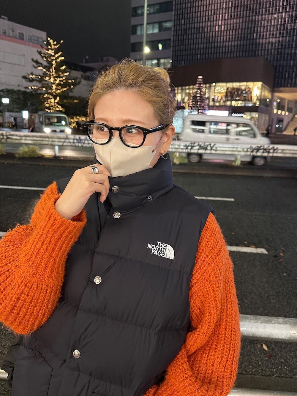 ブラウン系のスカート、ブラック系のダウンベスト、オレンジ系のニット/セーターを着用したレディースの冬コーディネートの2枚目の写真