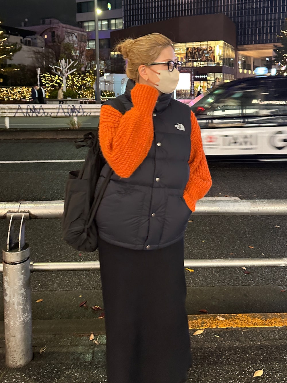 ブラウン系のスカート、ブラック系のダウンベスト、オレンジ系のニット/セーターを着用したレディースの冬コーディネートの3枚目の写真